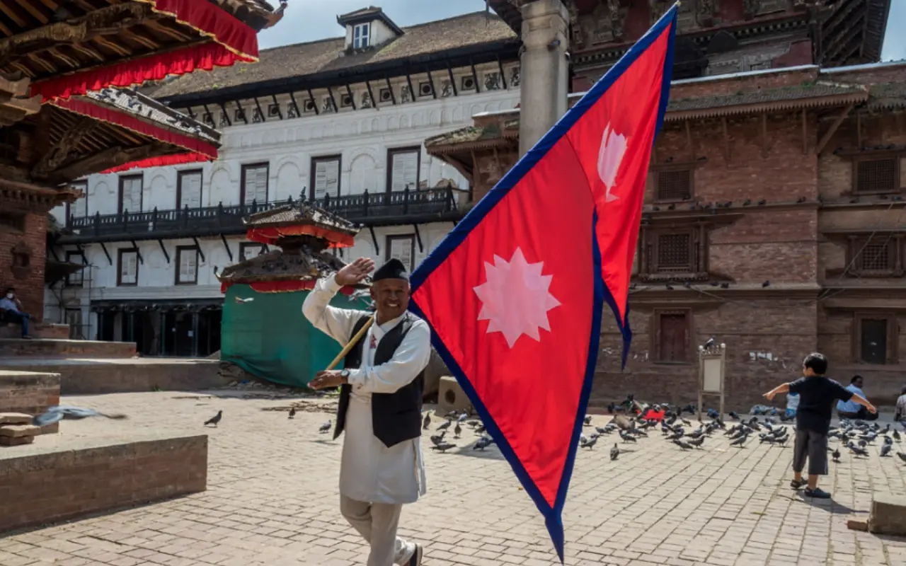A proud man holds high the unique Nepalese flag, a symbol of national pride and identity.
